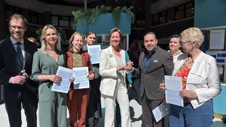 Voorzitter Mohammed Mohandis ontvangt een miniatuurstoel uit handen van Tessa Roseboom. Een selectie van de leden van de Kamercommissie van VWS hebben het manifest in handen.   